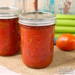 three jars filled with tomato sauce sitting on top of a table next to some vegetables