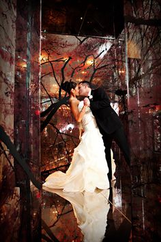 a bride and groom are kissing in front of a tree with red leaves on it