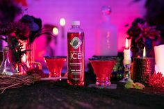 a bottle of booze next to some glasses and candles on a table with flowers