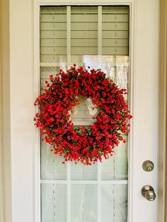 a wreath on the front door with red flowers hanging from it's side window