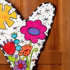 a painted heart hanging on the side of a wooden door with flowers and sunbursts