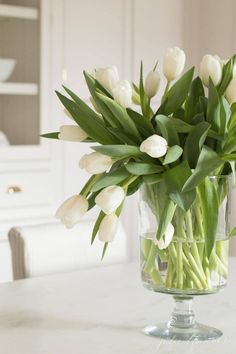 white tulips are in a clear vase on a marble table top with water