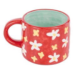 a red mug with yellow and white flowers on it's side, sitting in front of a white background