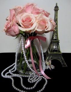 pink roses and pearls in a glass vase with a pearl necklace on the table next to the eiffel tower