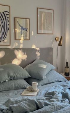 a bed with blue linens and pillows in a white room next to pictures on the wall