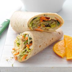 there is a wrap that has been cut in half and orange slices on the side