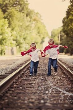 two young boys running down train tracks with their arms in the air and holding hands