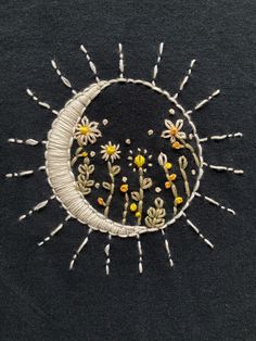 an embroidered sunburst with daisies in the center on a black shirt background