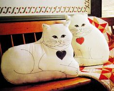 two pillows with cats on them are sitting on a wooden bench next to each other