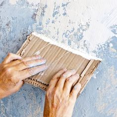 two hands are working on a piece of cardboard