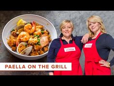 two women in red aprons standing next to a bowl of food and the words paella on the grill