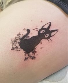 a black cat tattoo on the side of a woman's thigh with flowers around it