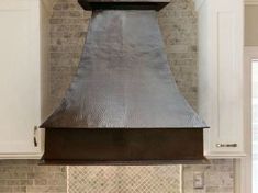 a kitchen with white cabinets and a large metal hood over the stove in front of an oven