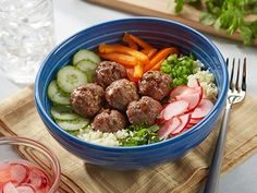 a blue bowl filled with meatballs and veggies next to a glass of water