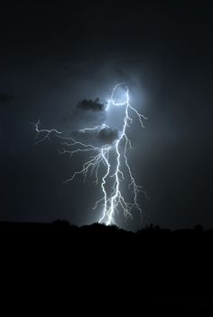 a lightning bolt is seen in the night sky over a hill and tree line with dark clouds