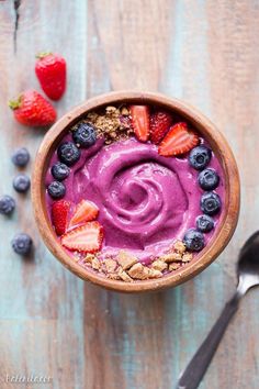 a bowl filled with fruit and yogurt next to spoons on a wooden table