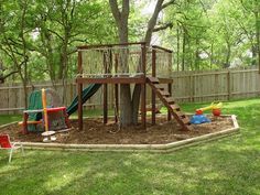 a play set in the middle of a yard next to a tree with toys on it