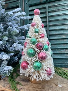 a small christmas tree made out of yarn on a wooden table next to some trees