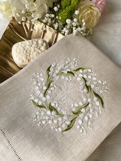 the embroidered monogram on this handkerchief is made with white flowers and green leaves, along with a gold plate