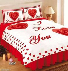 a bed with red hearts and i love you written on the comforter, next to a lamp