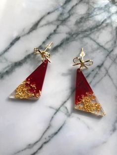 Handmade item Drop length: 5.5 Centimetres; Width: 1.7 Centimetres Materials: resin, gold plated, gold leaf Closure: Ear wire Made to Order Description Triangle resin dangle earrings, red and gold leaf. Each piece is made to order and the finished product may slightly vary from the photo. Each item is distinctive, special, and unique. Handmade Gold Earrings For Christmas, Handmade Gold Christmas Earrings, Gold Dangle Earrings For Holiday, Gold Jewelry With Matching Earrings For Holiday, Red Gold Plated Earrings For Party, Red Resin Drop Earrings, Gold Resin Jewelry With Ear Wire, Elegant Resin Earrings As Gift, Holiday Gold Earrings With Ear Wire