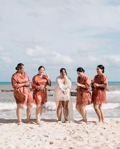 a group of women standing on top of a sandy beach next to the ocean in orange robes