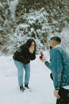 two people standing in the snow and one is holding something up to her face with both hands