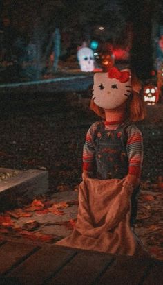 a hello kitty doll is standing on the ground in front of some pumpkins at night