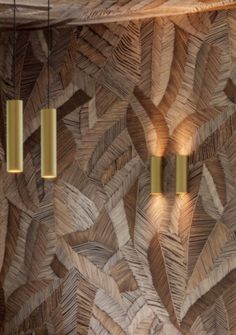 three lights hanging from the ceiling in front of a wooden wall with leaves on it