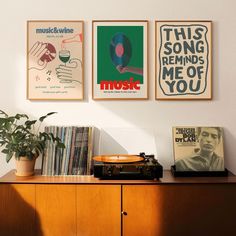 there are three posters on the wall above a record player and a potted plant