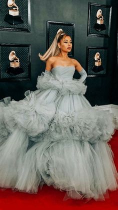 lady in grey gown standing on red carpet with her hands behind her back and head tilted to the side