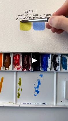 a person is holding a paintbrush and some watercolors in front of them