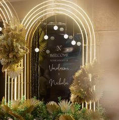 a welcome sign is displayed in front of an arch decorated with flowers and greenery