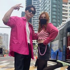 a man and woman standing next to each other in front of a bus on the street