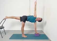 a man doing yoga on a blue mat in front of a chair with one leg up