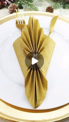 a gold plate topped with a folded napkin and fork next to an empty piece of paper