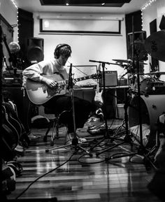 a man sitting in front of a guitar on top of a hard wood floor next to microphones