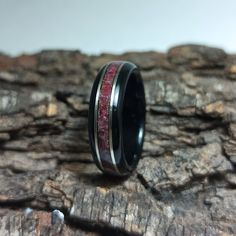 a wedding ring with red and black inlays sits on a piece of wood