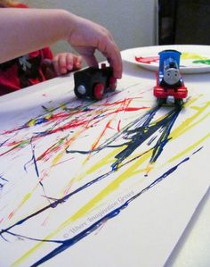 a child's hand is touching a train on a piece of paper with paint