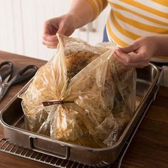 a person holding a plastic bag filled with food on top of a metal tray next to scissors