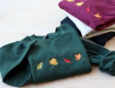 three different colored shirts with leaves on them sitting on the floor next to each other