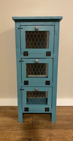 a small blue cabinet with chicken wire in the doors and drawers on each side, sitting on a hard wood floor