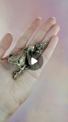 a small lizard brooch sitting on top of a person's hand in front of a pink background