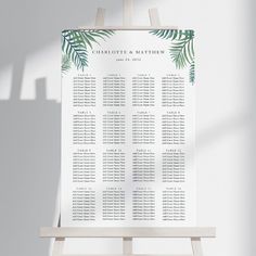 a wooden easer with a wedding seating chart on it and palm leaves in the background