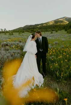 a bride and groom standing in a field with wildflowers at their wedding day