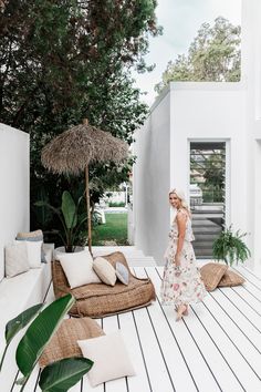 a woman in a dress standing on a deck next to a couch and umbrellas