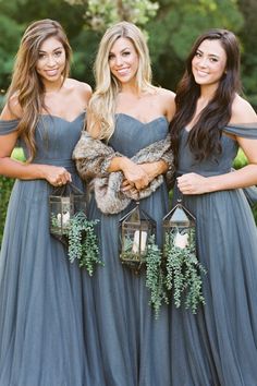 three bridesmaids in long grey dresses with fur stolers and lanterns hanging from them