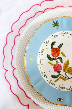 a plate with flowers painted on it sitting on a white table cloth next to another plate