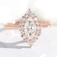 an oval cut diamond surrounded by smaller round diamonds on a rose gold band, sits atop a plain white surface