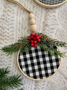 two christmas ornaments hanging on the wall with pine needles and red berries, one in black and white checkerboard